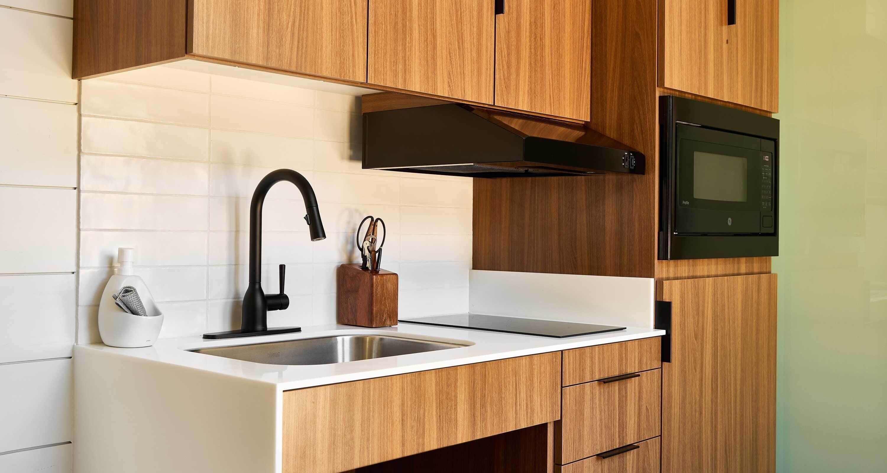 Una cocina moderna con armarios de madera, un lavamanos de acero inoxidable, un grifo negro y un microondas.