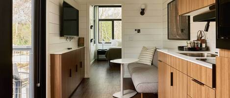 A compact kitchen with wooden cabinets, a built-in TV, and a small dining area with a table and bench.