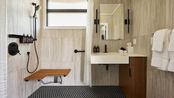 A modern bathroom with a shower, sink, mirror, and wooden bench.