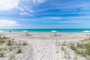 A beach with white sand, clear blue water, and a few umbrellas.