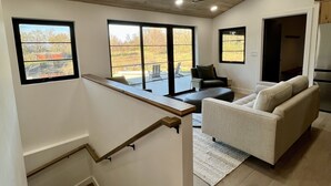 Un intérieur moderne avec un escalier en bois, un espace de vie doté d’un canapé et de grandes fenêtres offrant une vue sur l’extérieur.