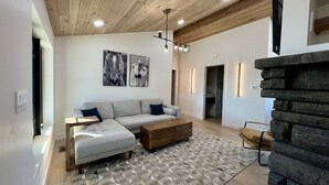 Un salon moderne avec un plafond en bois, un canapé gris, un tapis à motifs et une cheminée en pierre.