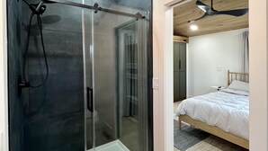 Une salle de bain moderne avec une douche à parois de verre, un plafond en bois et des toilettes apparentes.