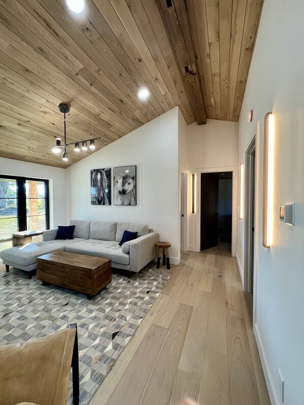 A modern living room with a sectional sofa, a wooden coffee table, and a geometric rug. There are two wall-mounted light fixtures and a ceiling light. - Completely remodeled luxury 3 bedroom, 3 bathroom House in quiet country setting (Hanna City)