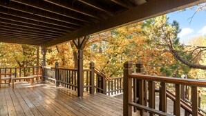 A wooden deck with railings, benches, and a view of autumn trees.
