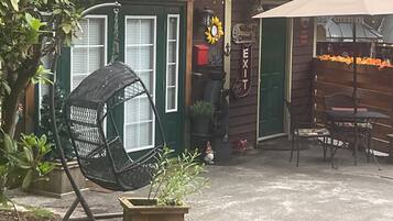 Un edifici rústic amb una porta verda, una cadira bressol, una taula amb cadires i una petita zona de jardí.