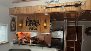 A kitchen with wooden paneling, a 'Home Sweet Home' sign, a refrigerator, and a ladder.