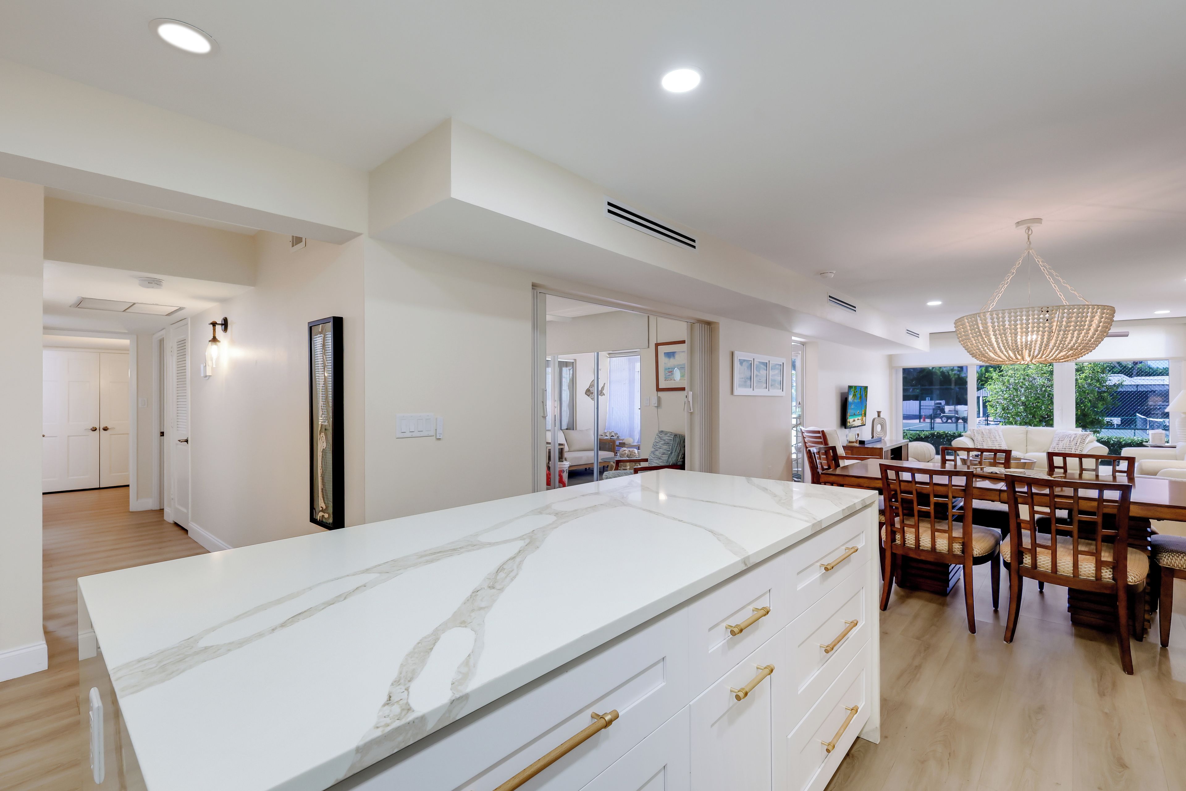 A modern kitchen with a marble countertop, wooden chairs, and a dining area with a chandelier.