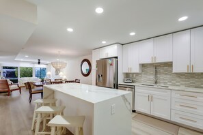 A modern kitchen with white cabinetry, a marble island, and a dining area with a chandelier. - Beach lovers dream (Longboat Key)