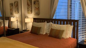 A neatly made bed with a brown bedspread and a yellow throw blanket, a bedside table with a lamp, and a window with blinds.