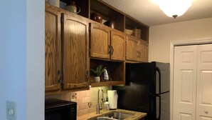 A kitchen with wooden cabinets, a black refrigerator, a granite countertop, and a stainless steel sink.