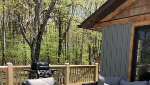 An outdoor deck with wicker furniture, a grill, and a view of the forest. - Hot tub-petfriendly-firepit-pool table-bar-3+acres (McHenry)