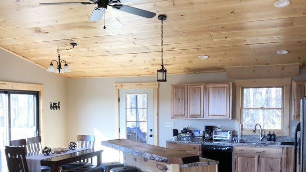 A spacious kitchen with wooden cabinets, a central island with stools, a ceiling fan, and a dining area with a table and chairs. - Hot tub-petfriendly-firepit-pool table-bar-3+acres (McHenry)