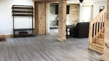 A spacious room with a wooden floor, a bench with hooks, a stone wall, and a staircase.