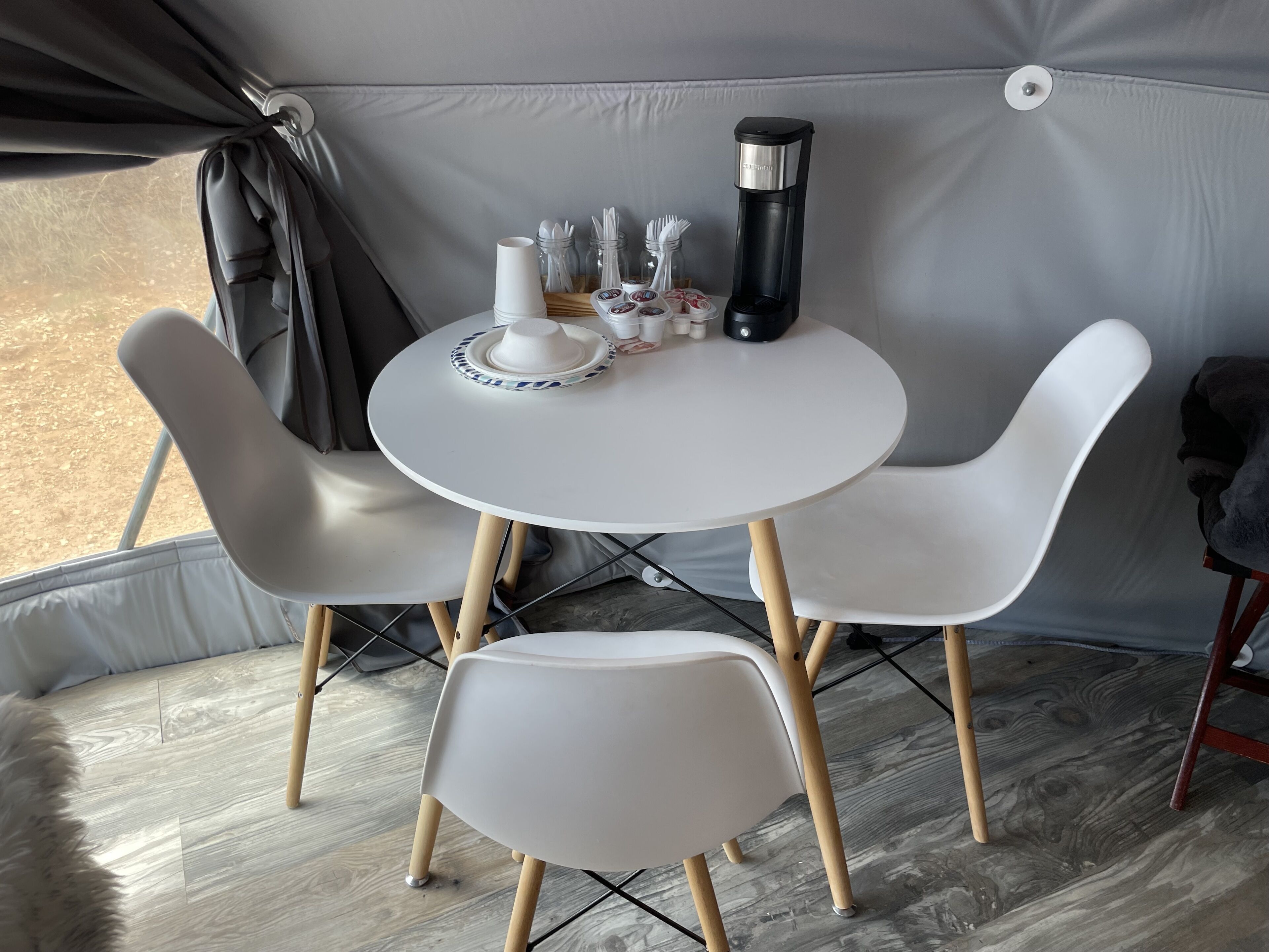 Une tente avec une table ronde et quatre chaises, une machine à café et une tasse sur la table.