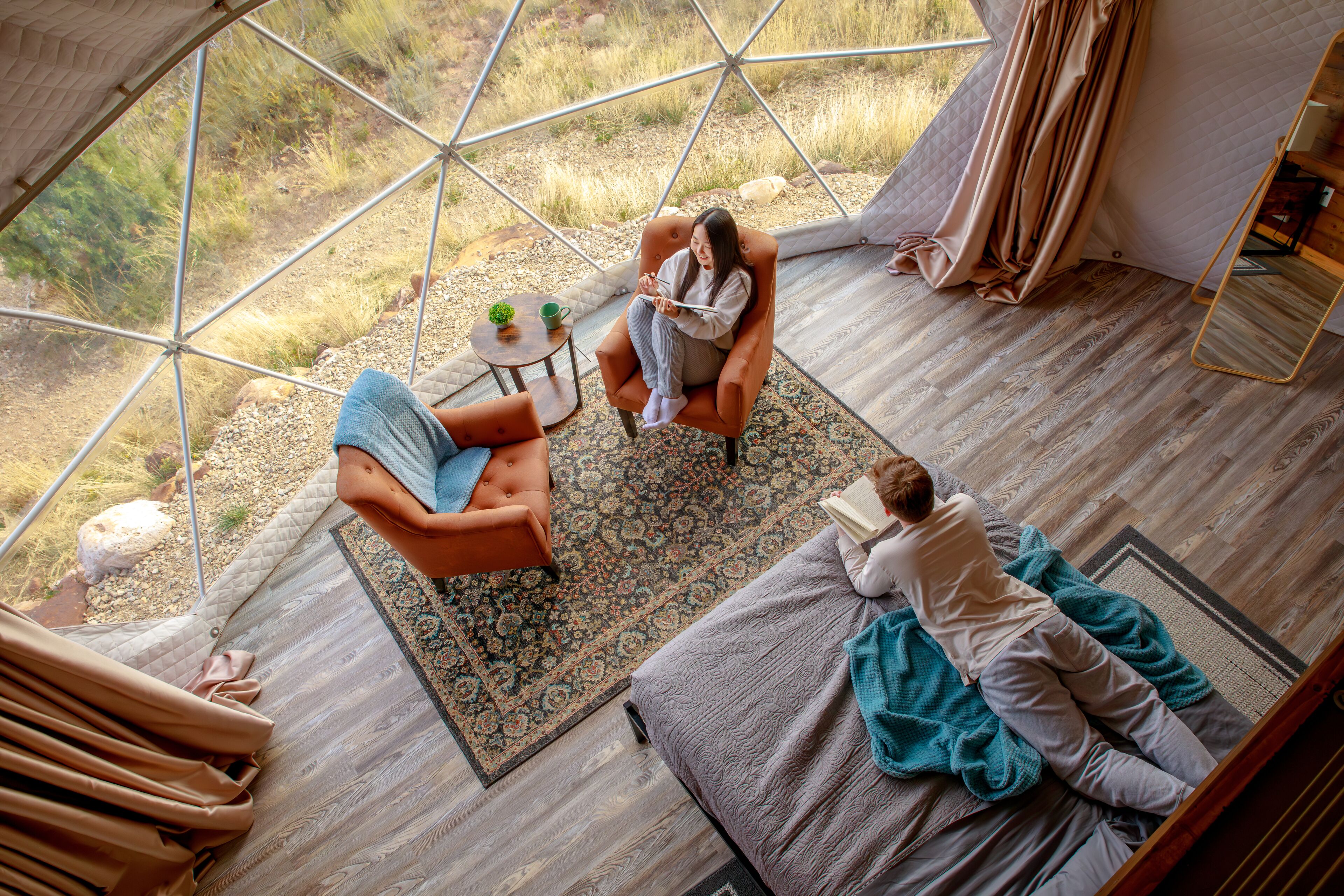 A spacious room with a large window, a cozy seating area with a patterned rug, and a wooden floor.