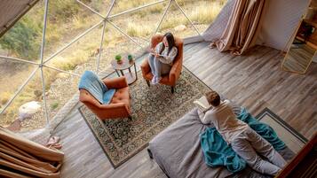 A spacious room with a large window, a cozy seating area with a patterned rug, and a wooden floor.