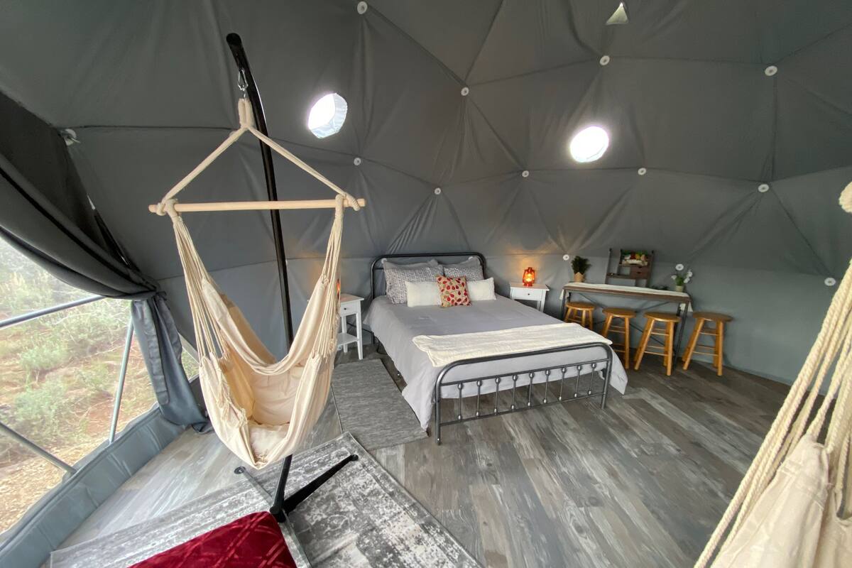 A tented accommodation with a bed, a desk, and a hanging chair.