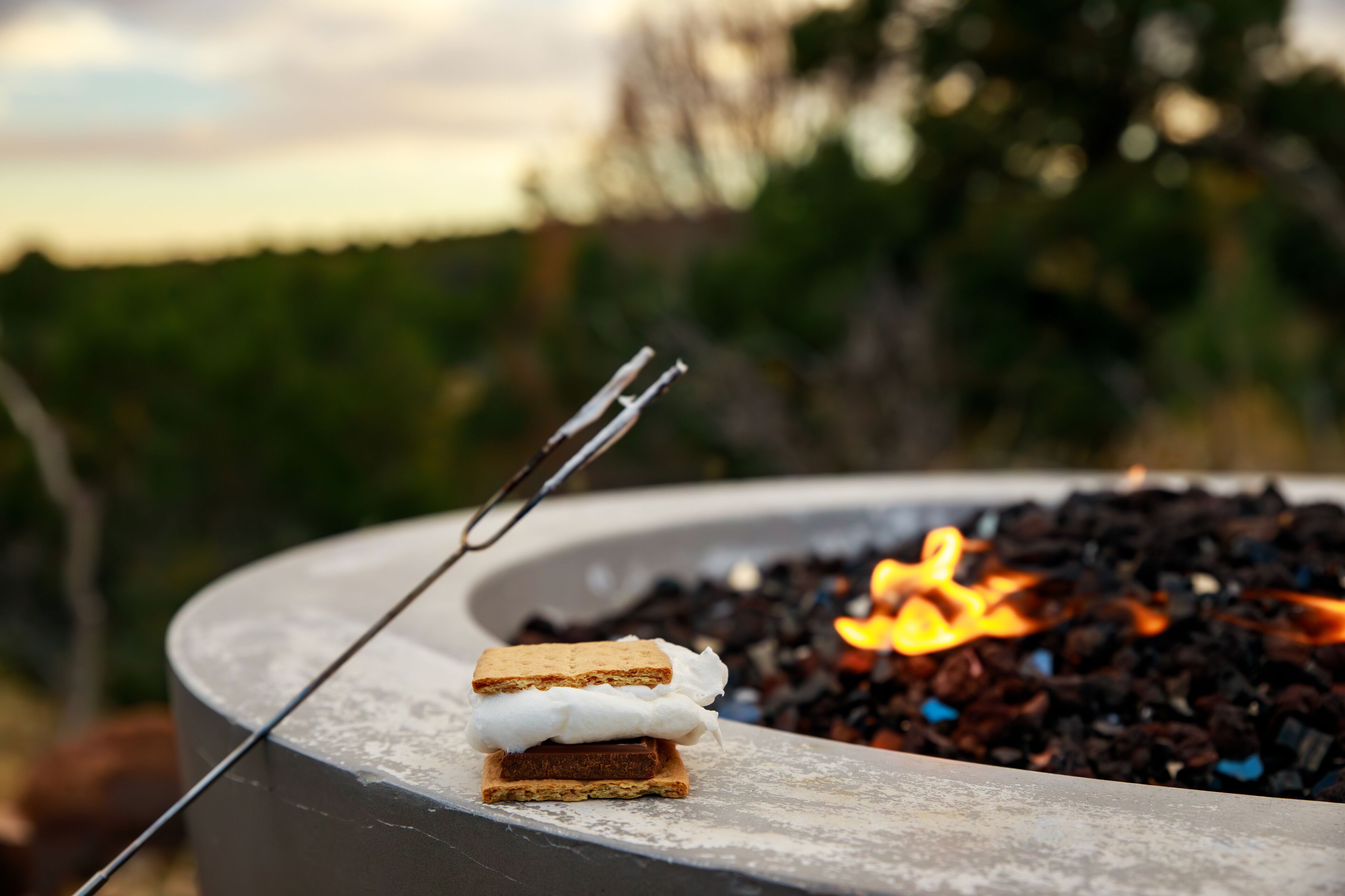 A campfire with a marshmallow on a stick, surrounded by a concrete fire pit.