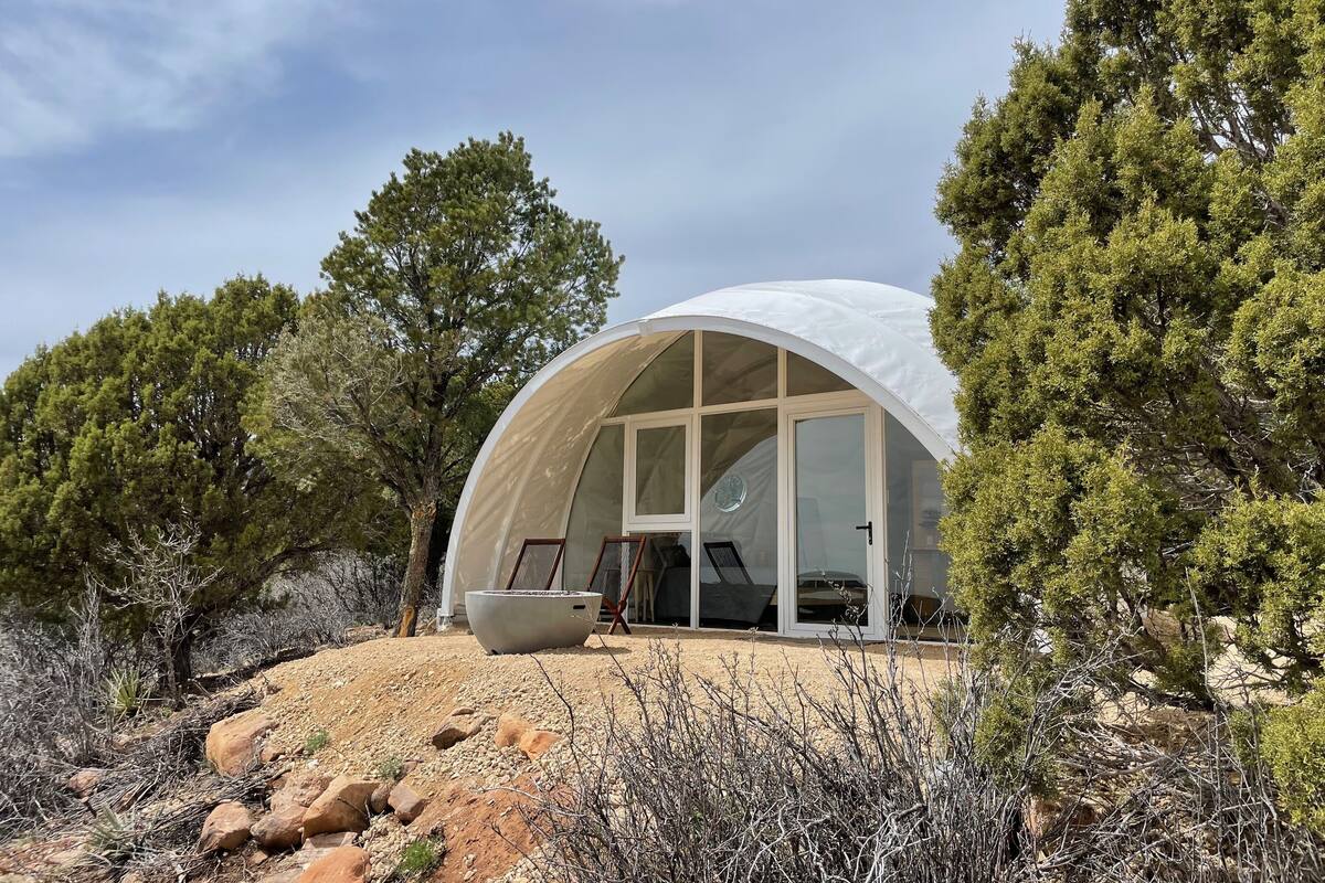 A dome-shaped structure with large windows, surrounded by trees and rocky terrain.