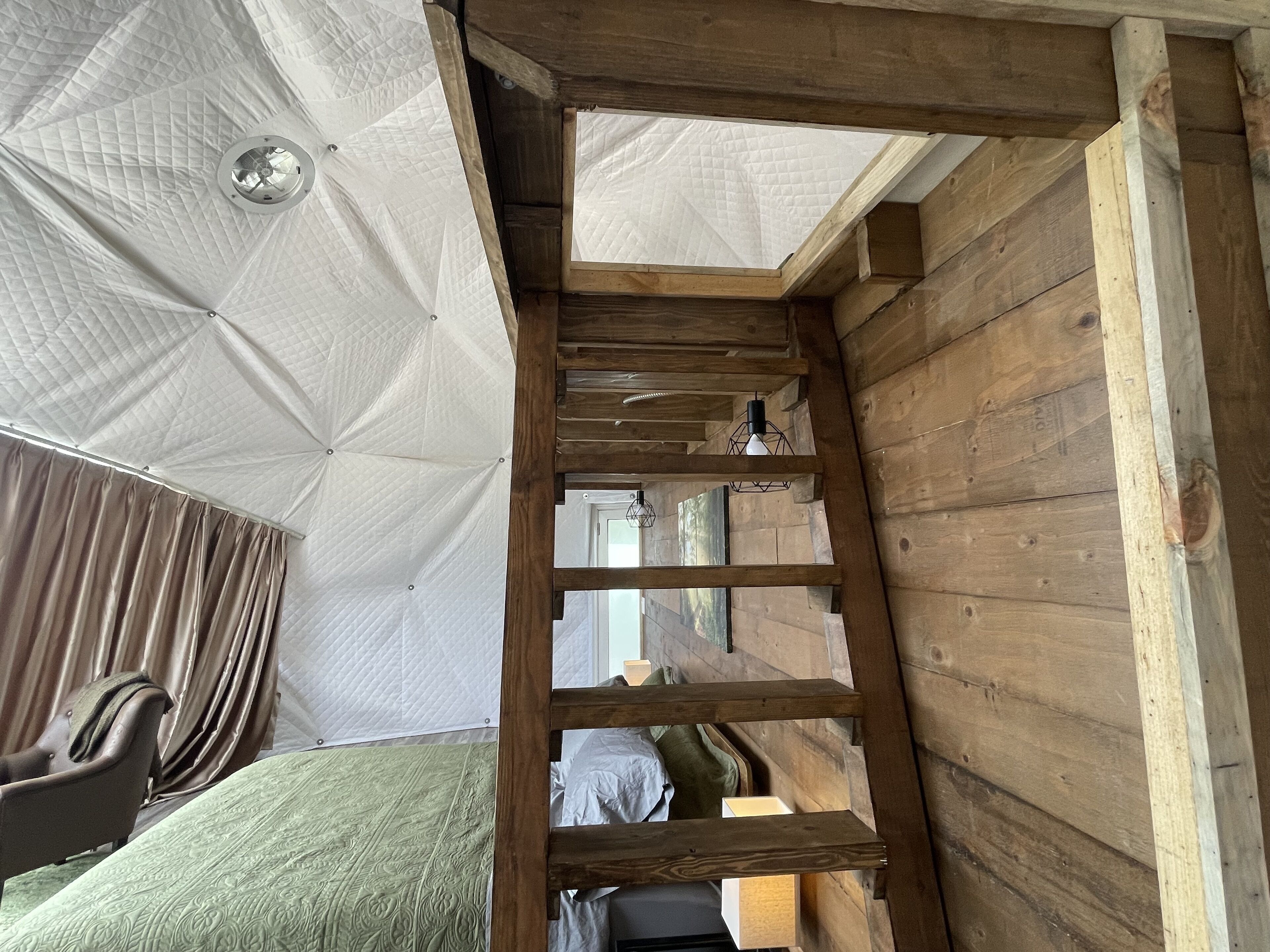 Een houten interieur met een stapelbed, een trapje en een plafond met een gewatteerd patroon.