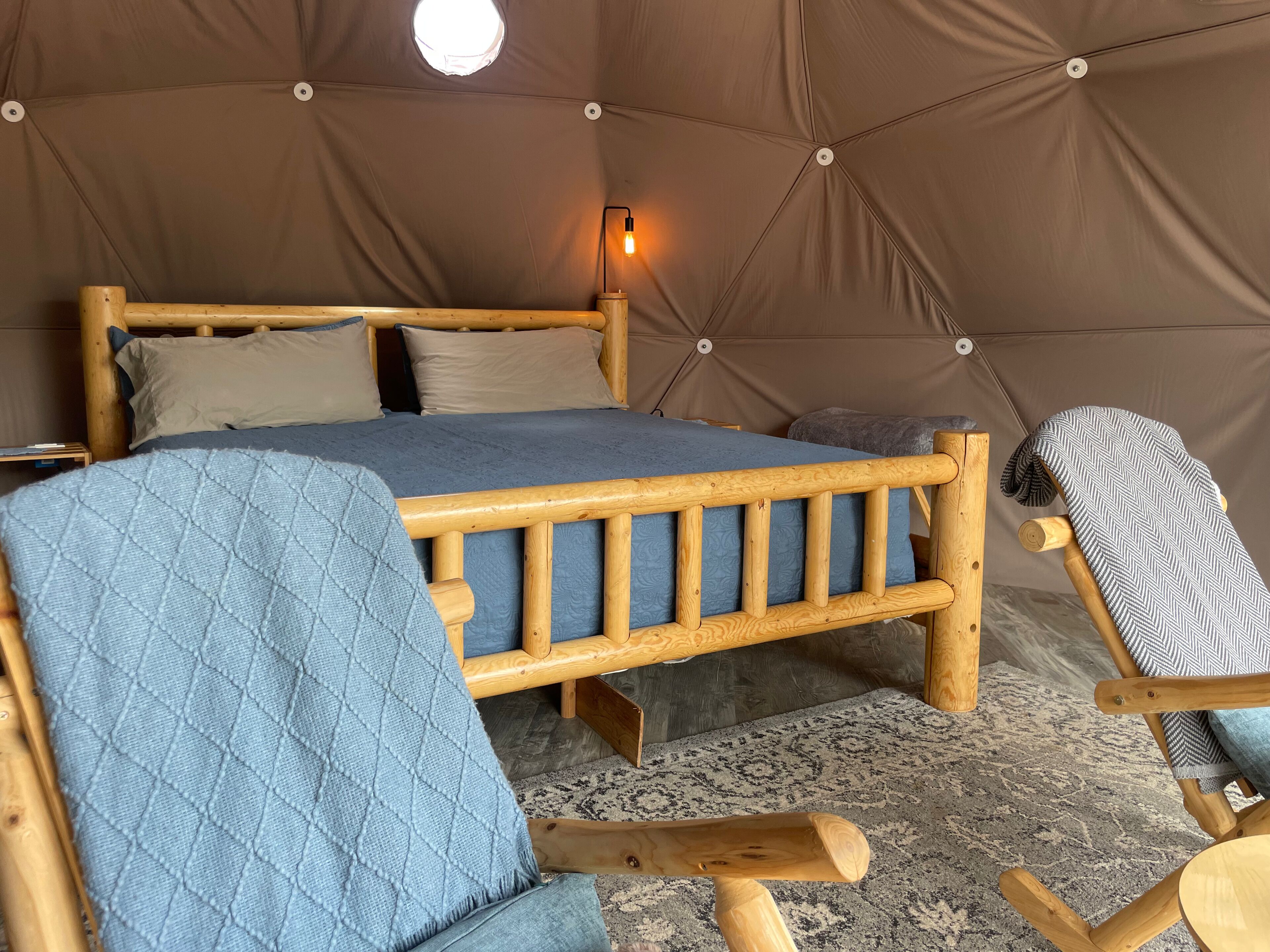A cozy tent-style room with a wooden bed, a blue quilted blanket, and a herringbone-patterned throw.