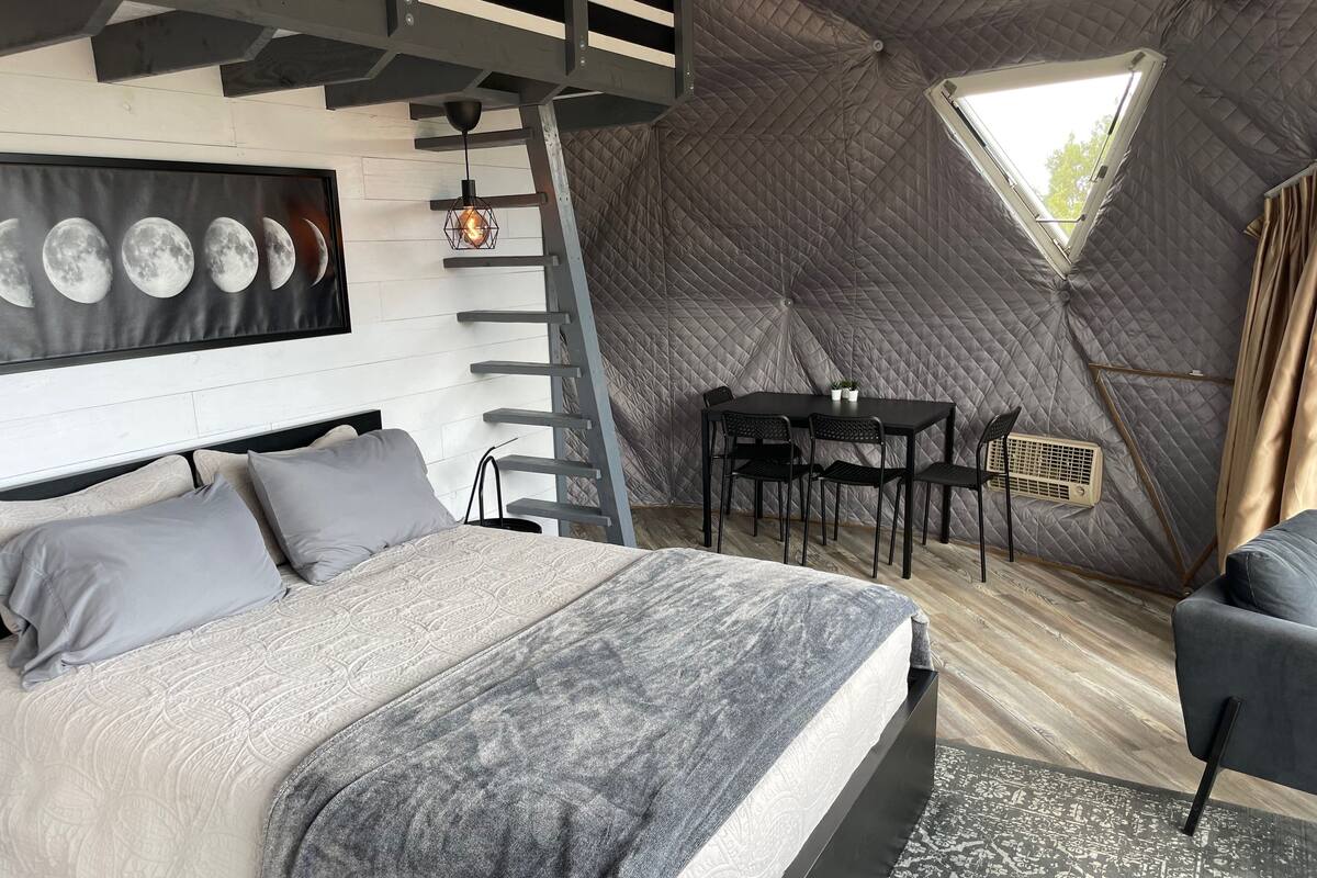 A tent-style room with a bed, a table with chairs, a ladder, and a window.