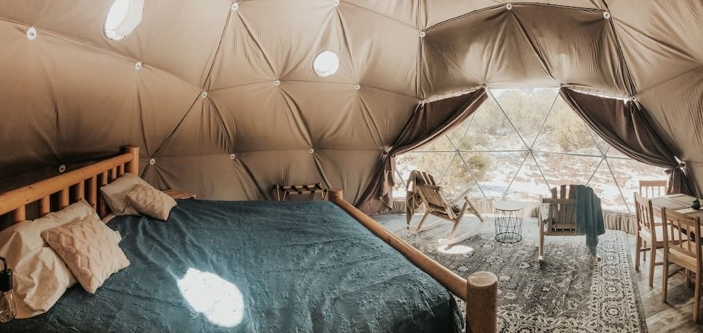 A tent with a bed, wooden furniture, and a view of the outdoors.
