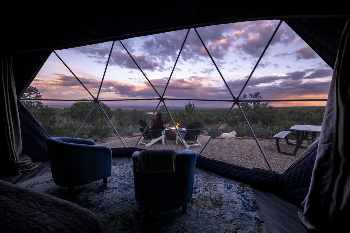 A cozy tent with a view of a sunset over a forested landscape.