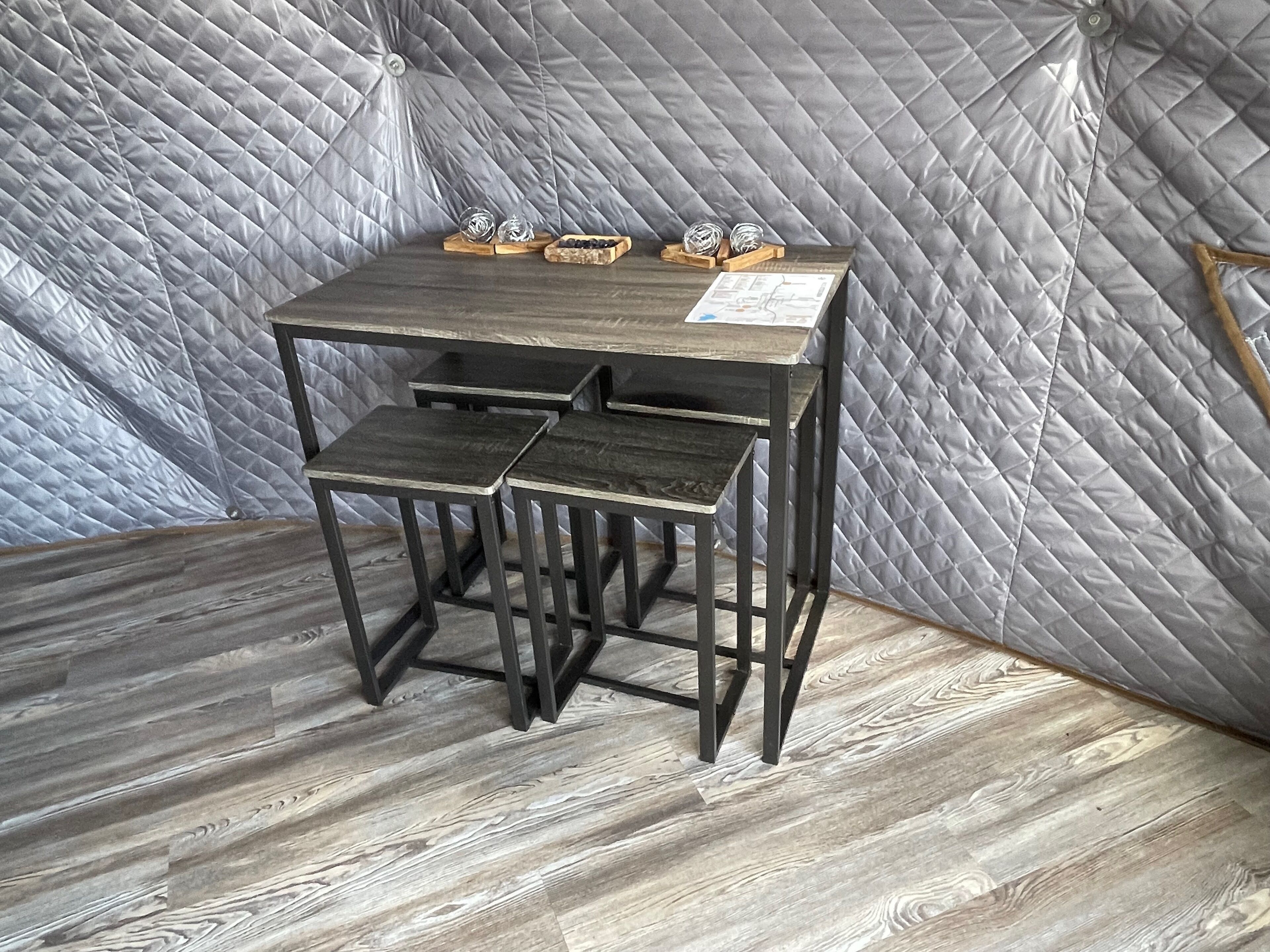 Une petite table en bois foncé, accompagnée d’un tabouret assorti, placée devant un mur gris matelassé et sur un plancher en bois.