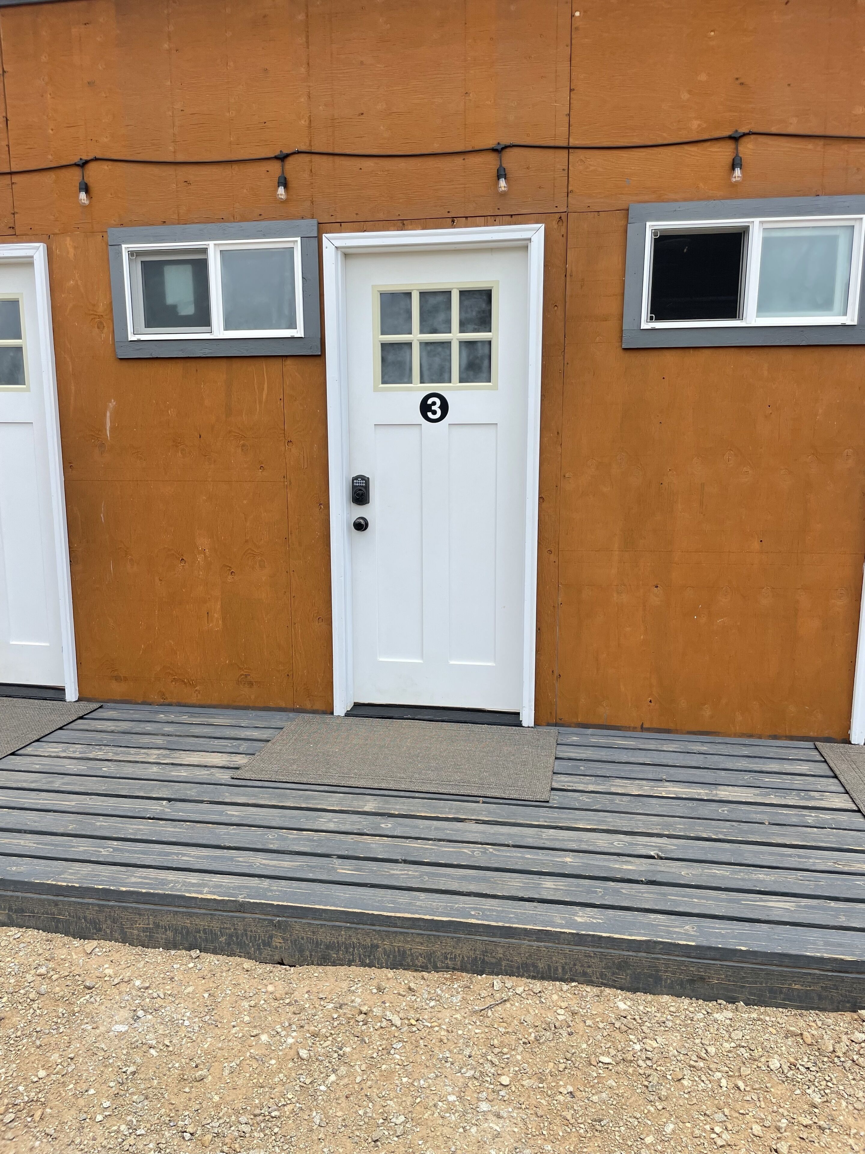 A white door with a number '3' above it, set in a wooden wall with two small windows above.