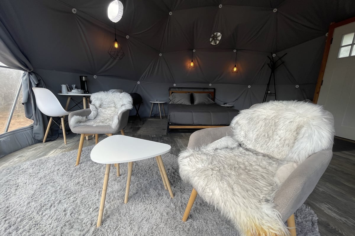 A cozy tented accommodation with a bed, two chairs, a small table, and a hanging light fixture.