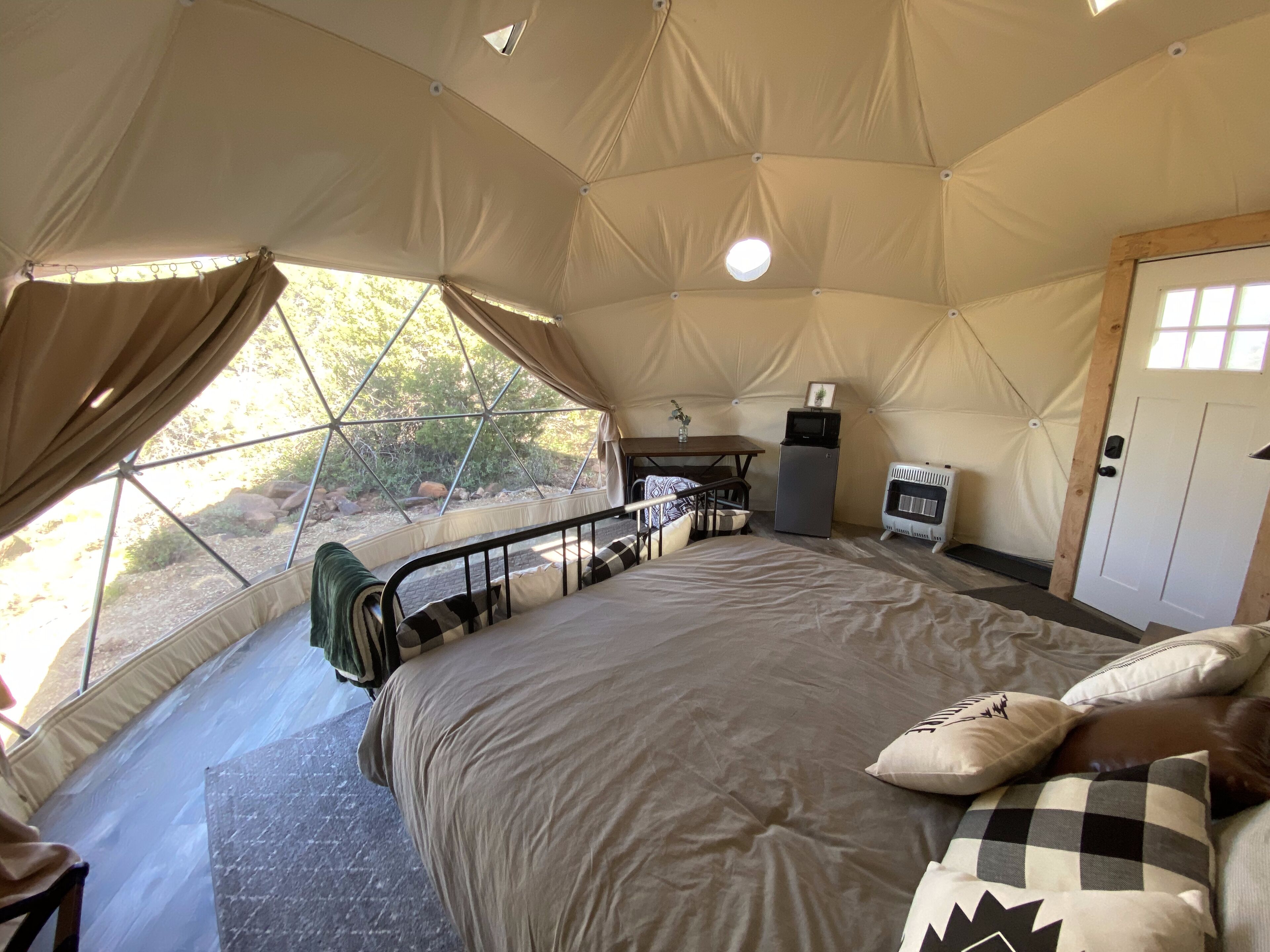 Una sistemazione in tenda con un letto, un piccolo tavolo, un frigorifero e una finestra vista aperta.