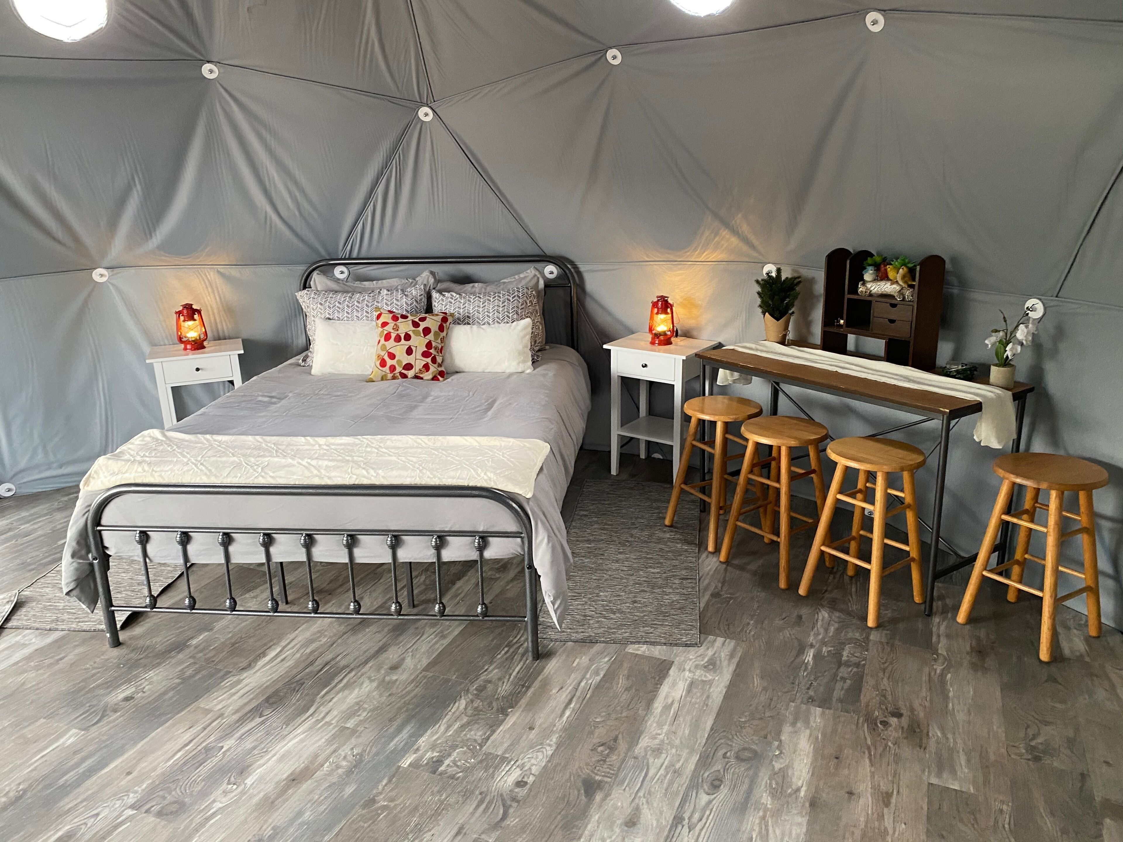 A tent-style bedroom with a bed, bedside tables, a desk with stools, and a small shelf with decorative items.