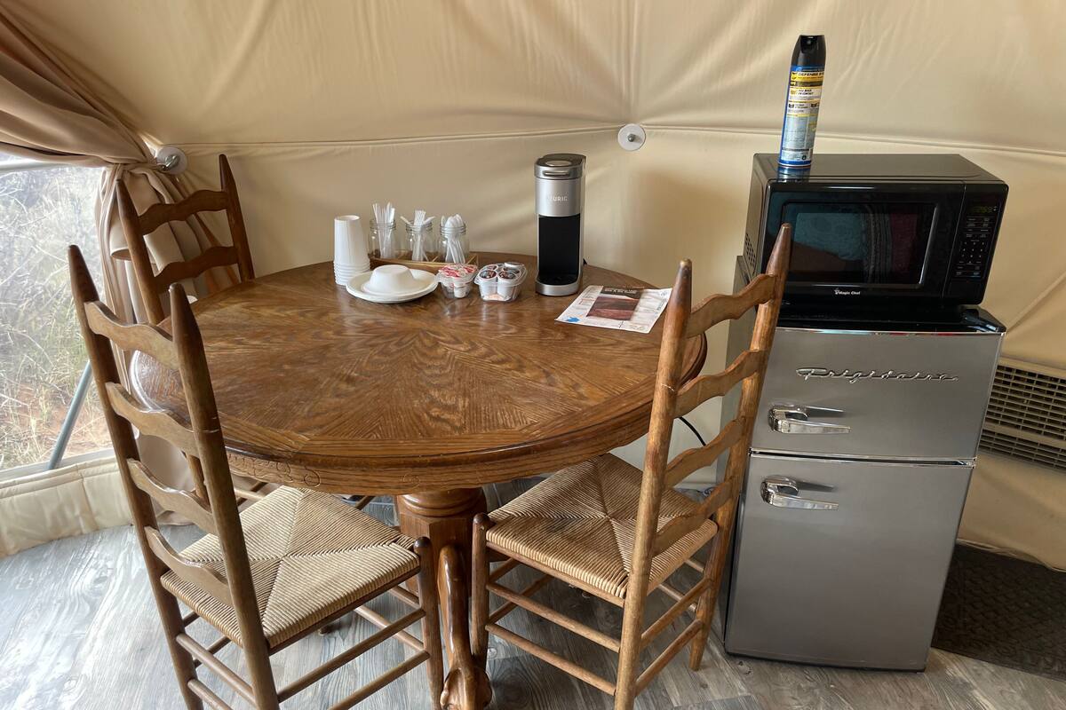 A compact kitchen with a wooden table, chairs, a refrigerator, and a microwave.