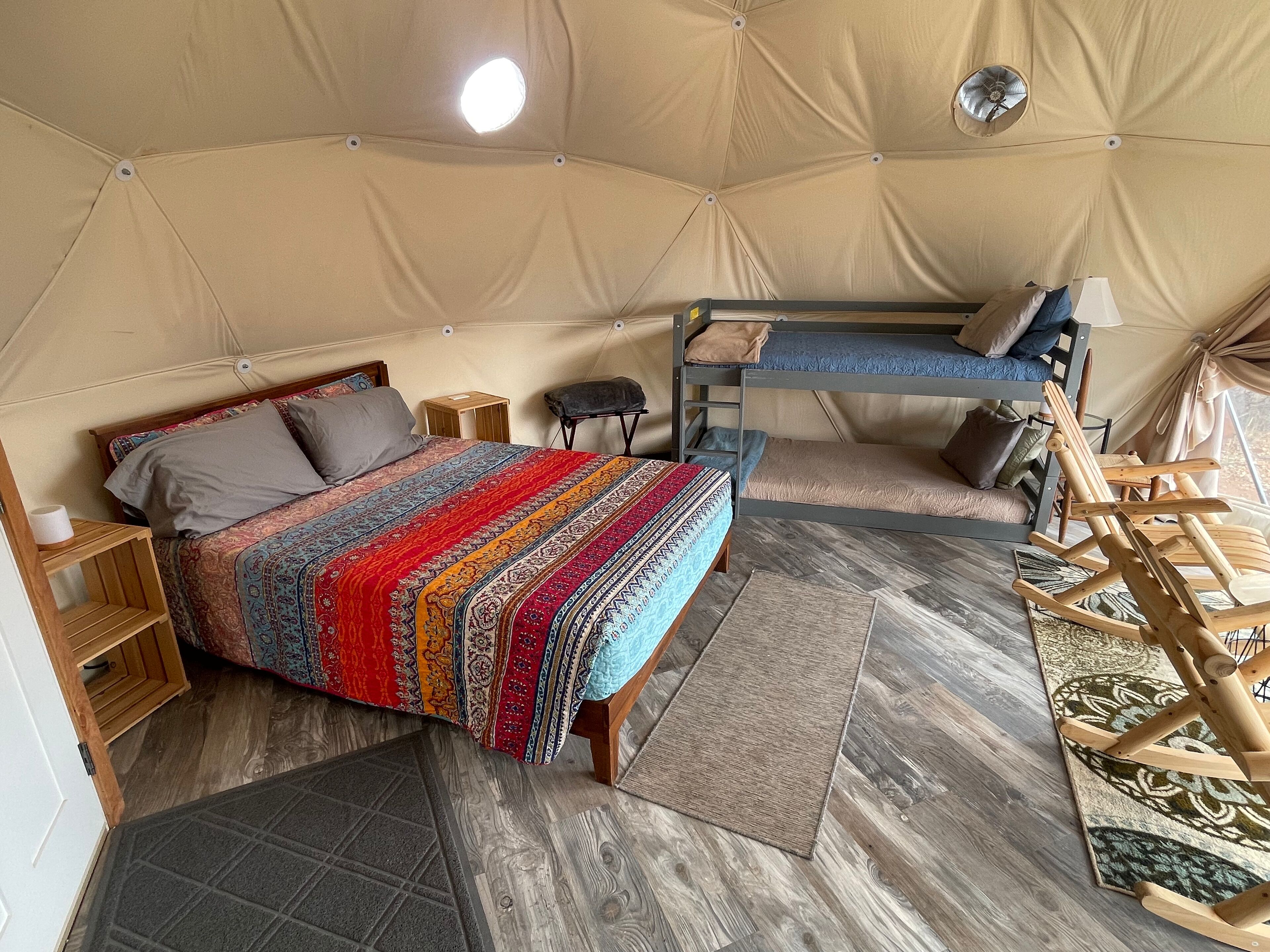 Alojamiento con carpa que incluye una cama litera, una cama individual con una manta estampada, una mesita de madera y una mecedora de madera.