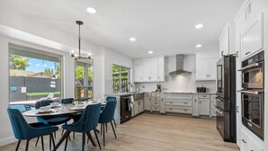 A modern kitchen with white cabinets, stainless steel appliances, and a dining area with blue chairs. - Scottsdale Paradise! Basketball, Heated Pool, Golf (Scottsdale)