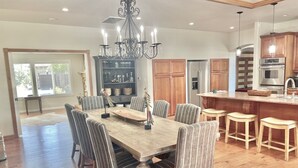 Un comedor espacioso con una gran mesa de madera y sillas a rayas, un candelabro, y una cocina con armarios de madera y electrodomésticos de acero inoxidable.