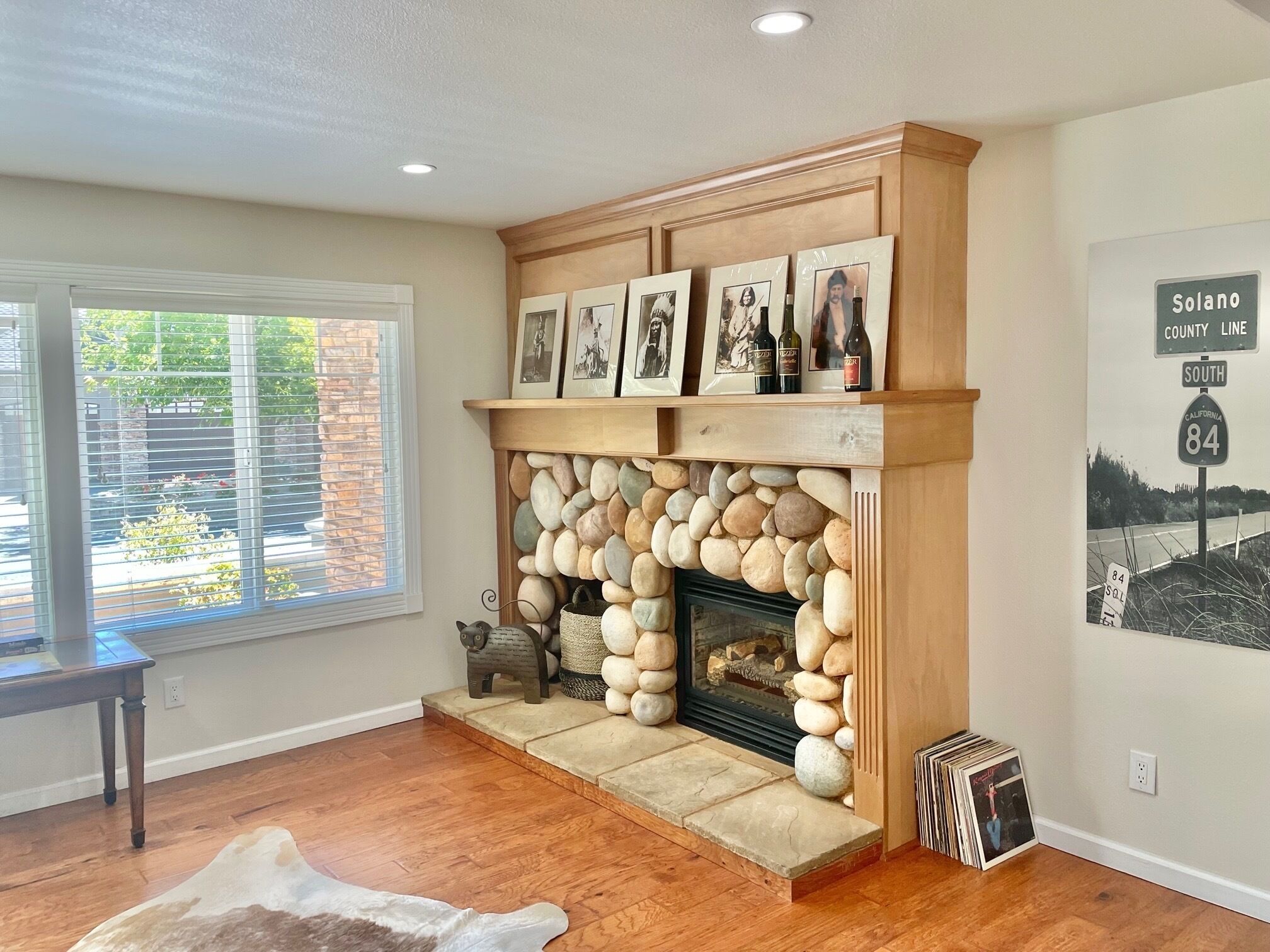 A living room with a stone fireplace, framed pictures, and a Solano County Line sign.