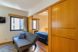 A modern hotel room with a sofa, a bed, and a wooden wardrobe.