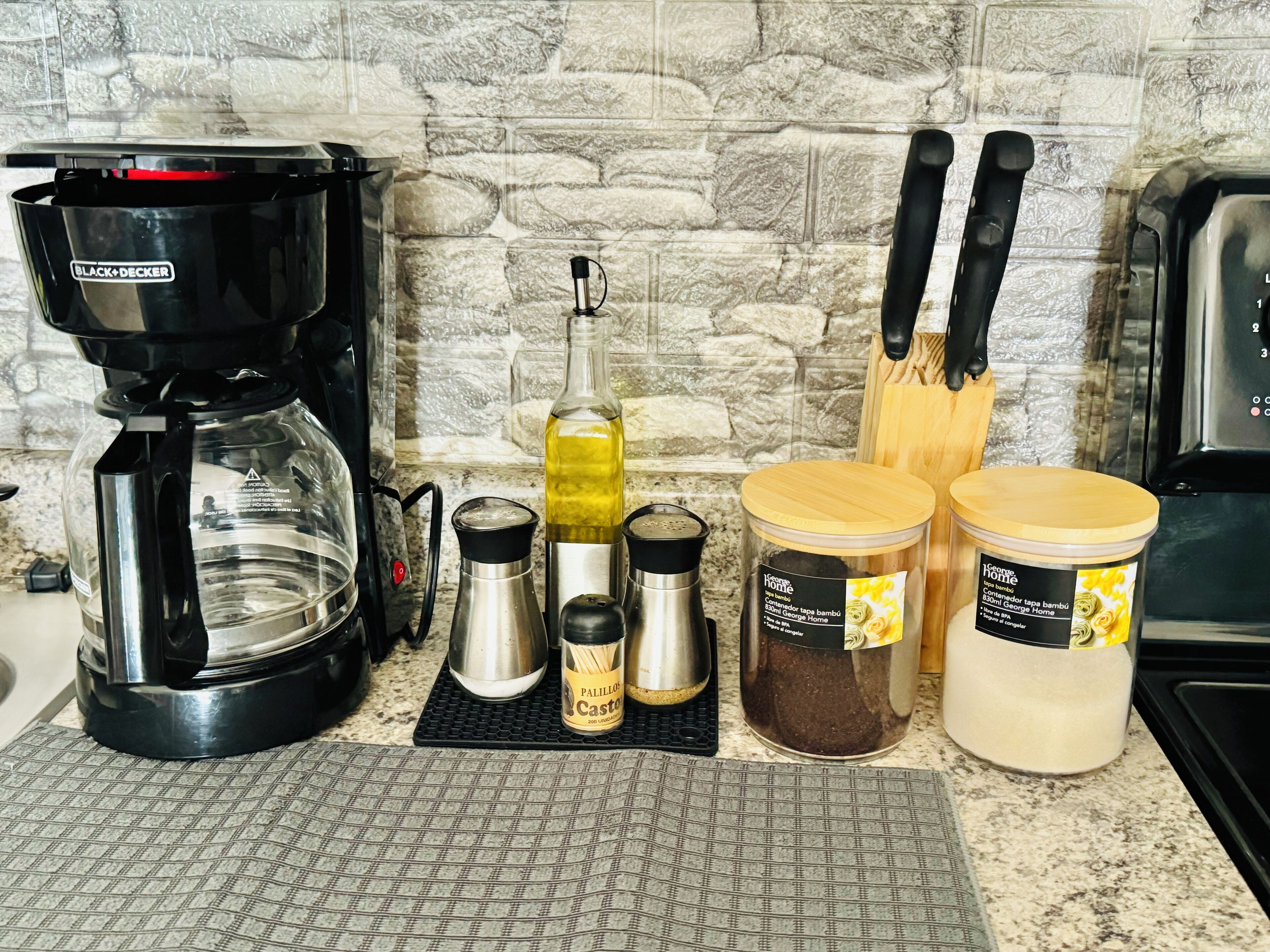 A kitchen counter with a coffee maker, a bottle of olive oil, and two jars of spices.