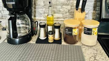 A kitchen counter with a coffee maker, a bottle of olive oil, and two jars of spices.