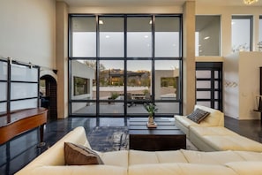 A spacious living room with a large window, a sofa, a coffee table, and a wooden bench. - Heated Pool / Mountain Views / Spa / 4 BR 3.5 BA (Tucson)