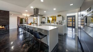 Cocina moderna con una isla central, taburetes de bar, chimenea y electrodomésticos de acero inoxidable.