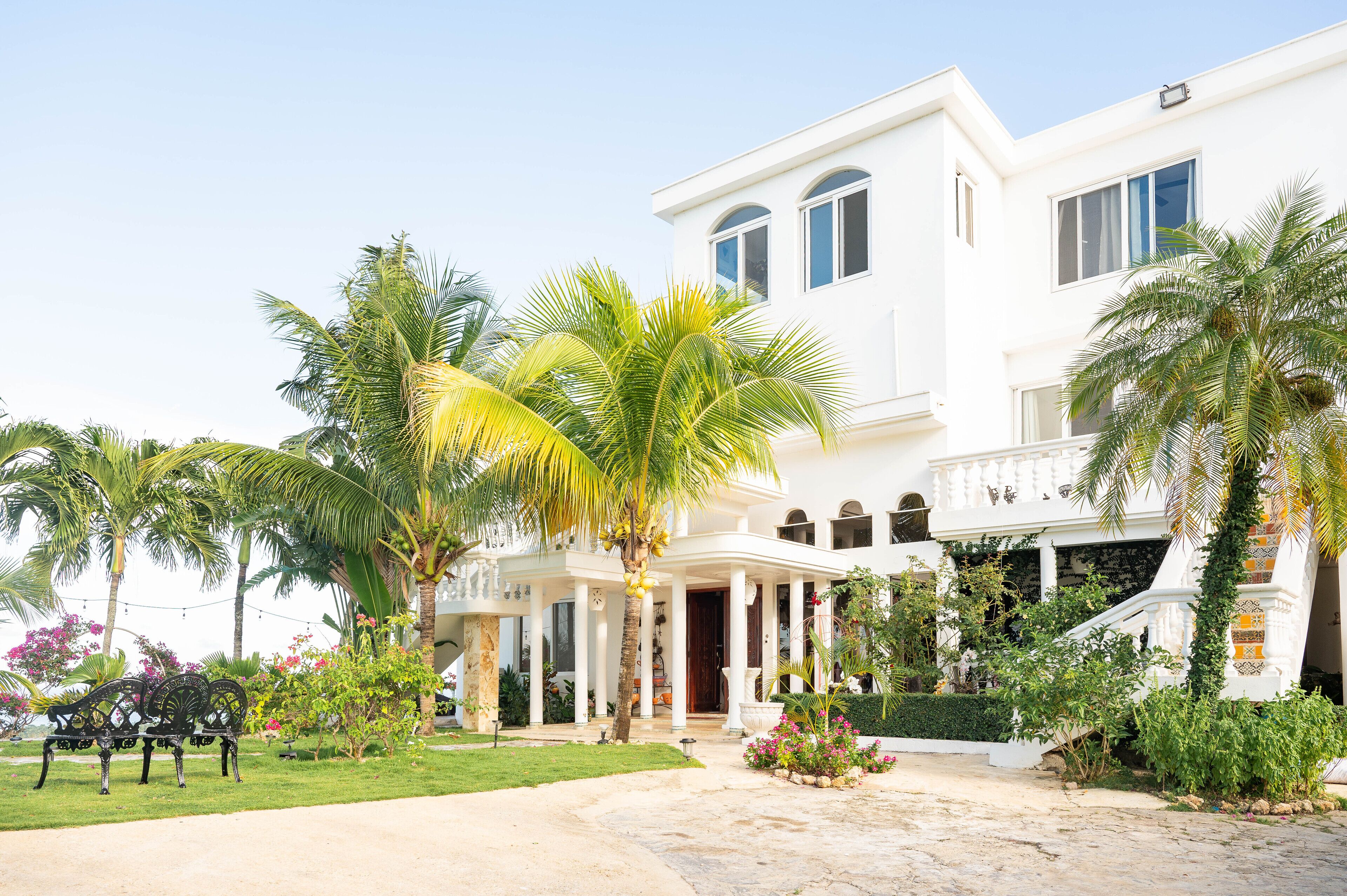 Un edificio blanco con porche cubierto, palmeras y un jardín cuidado.