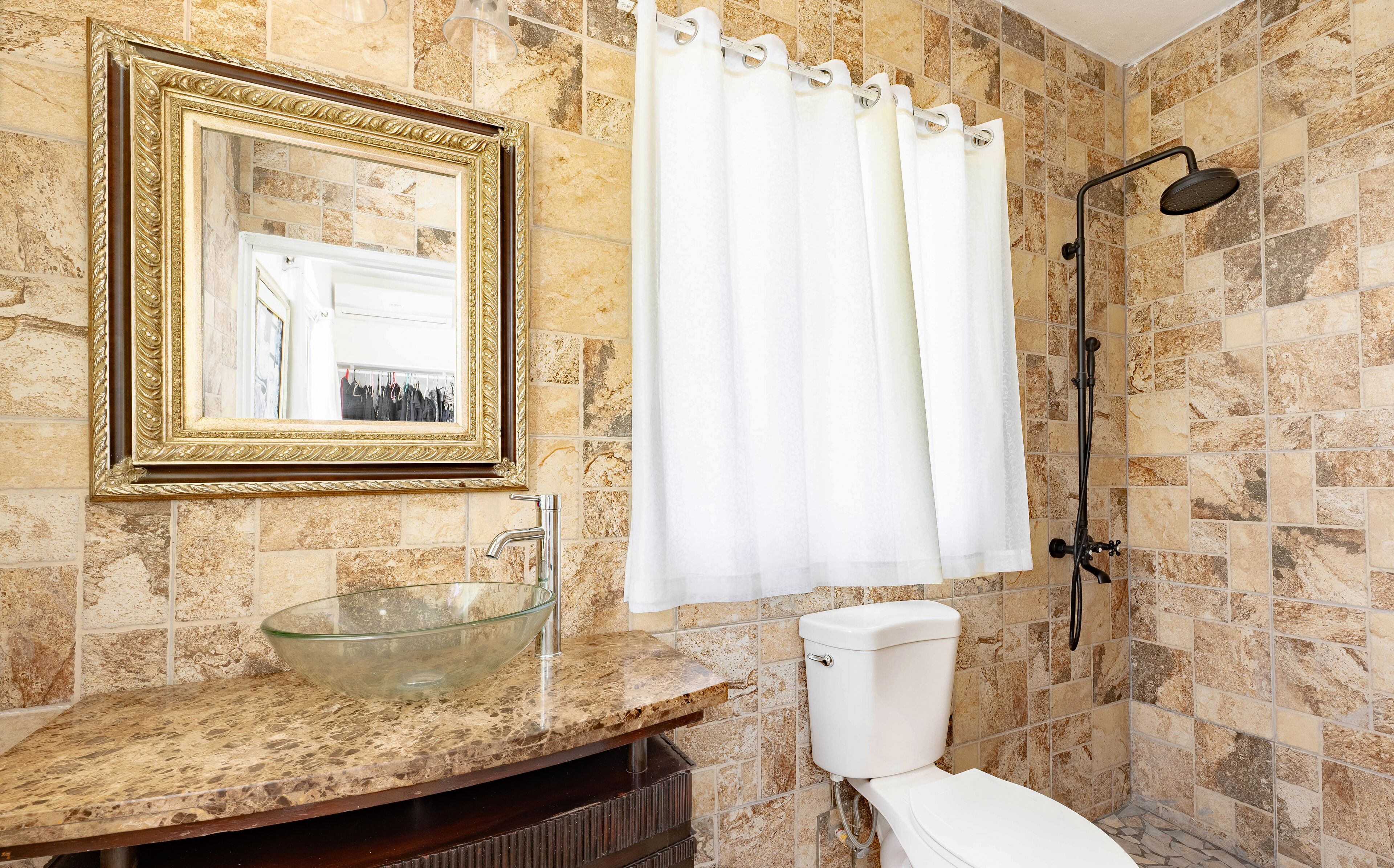 A bathroom with a marble sink, a toilet, a shower, and a large mirror with a gold frame.