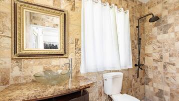 A bathroom with a marble sink, a toilet, a shower, and a large mirror with a gold frame.