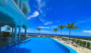 A pool with a clear view of the ocean, a covered area with columns, and a white railing with potted plants. - Casablanca Hotel (Cabrera)