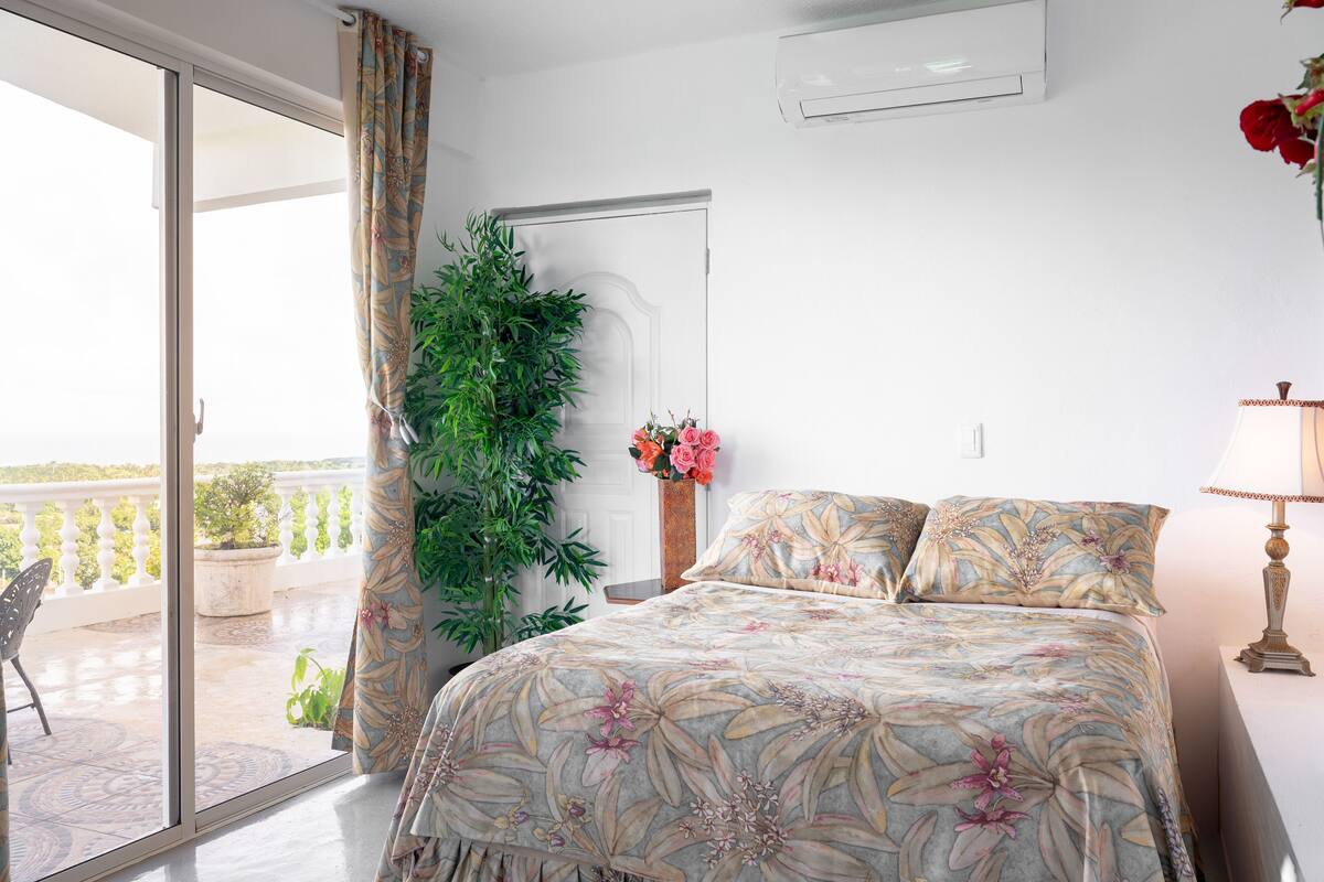 Un dormitorio con una cama, una planta en maceta, un florero con flores y vistas al balcón.