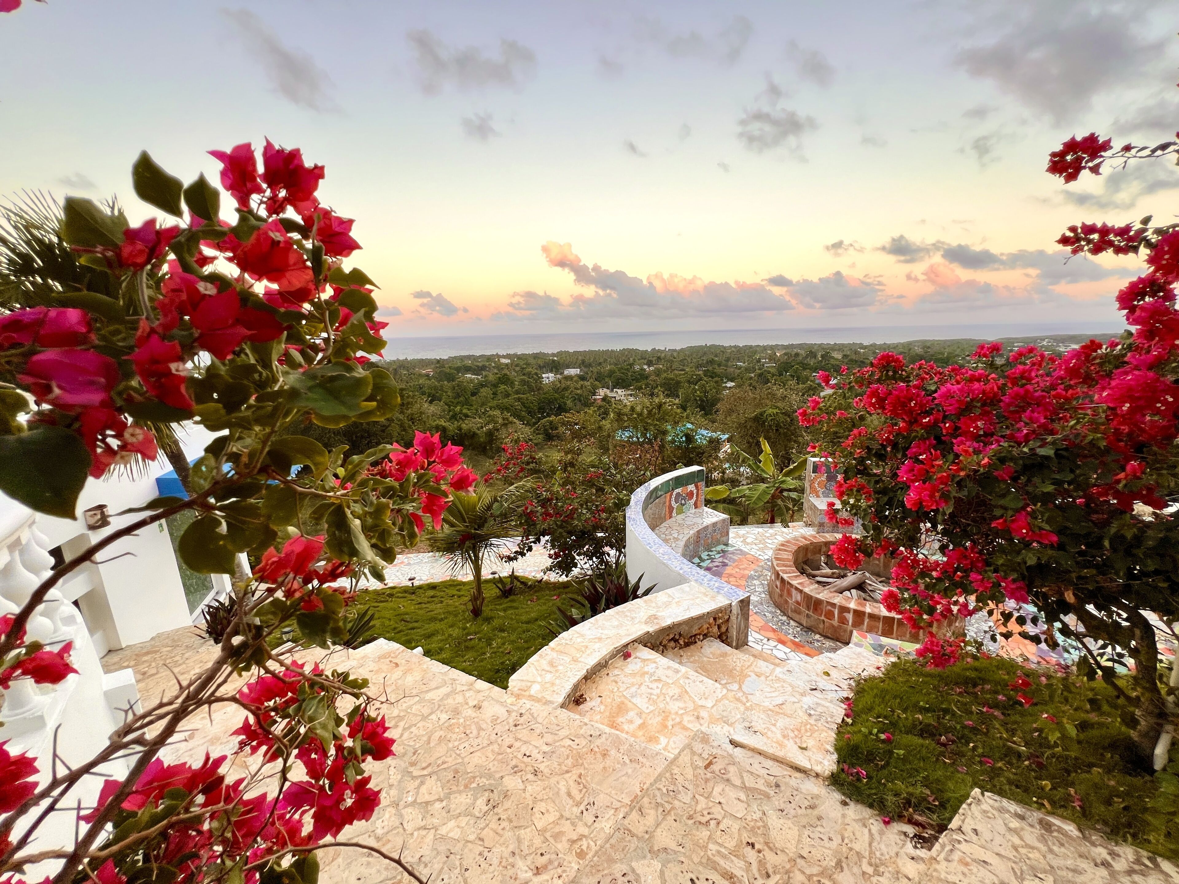 A view of a garden with a stone pathway leading to a tiled area with a view of the surrounding landscape.